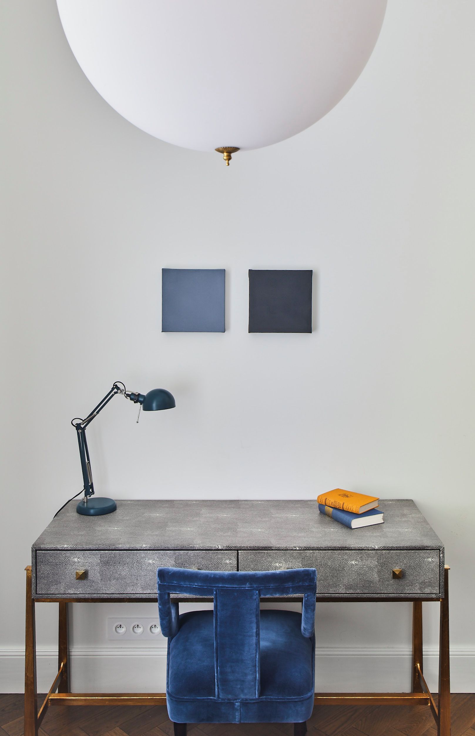 Un espace de travail comprenant un bureau, une chaise, une lampe et deux tableaux encadrés accrochés au mur.