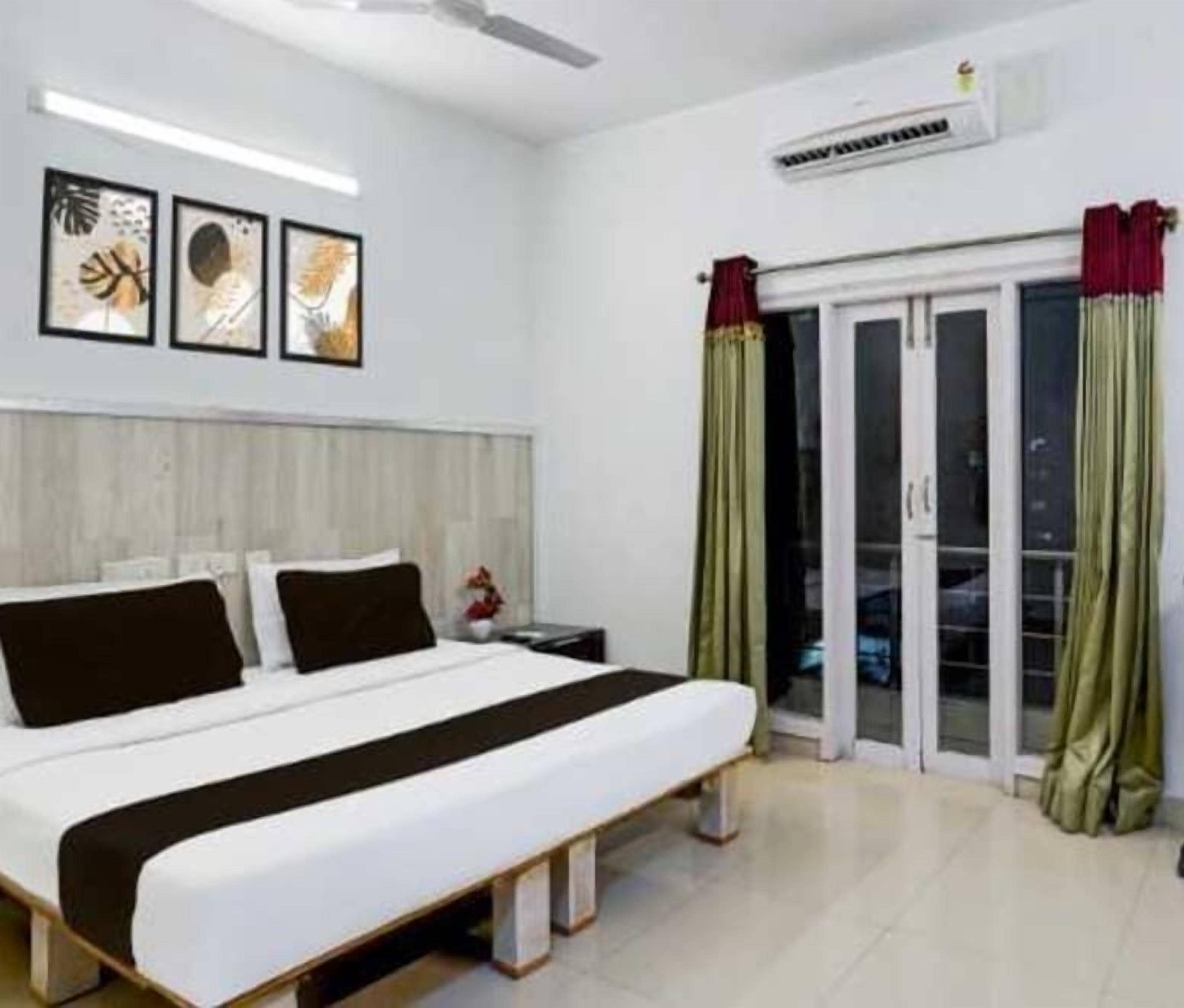 A bedroom with a bed, a nightstand, a window with curtains, and a wall-mounted air conditioner.