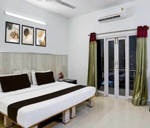 A bedroom with a bed, a nightstand, a window with curtains, and a wall-mounted air conditioner.