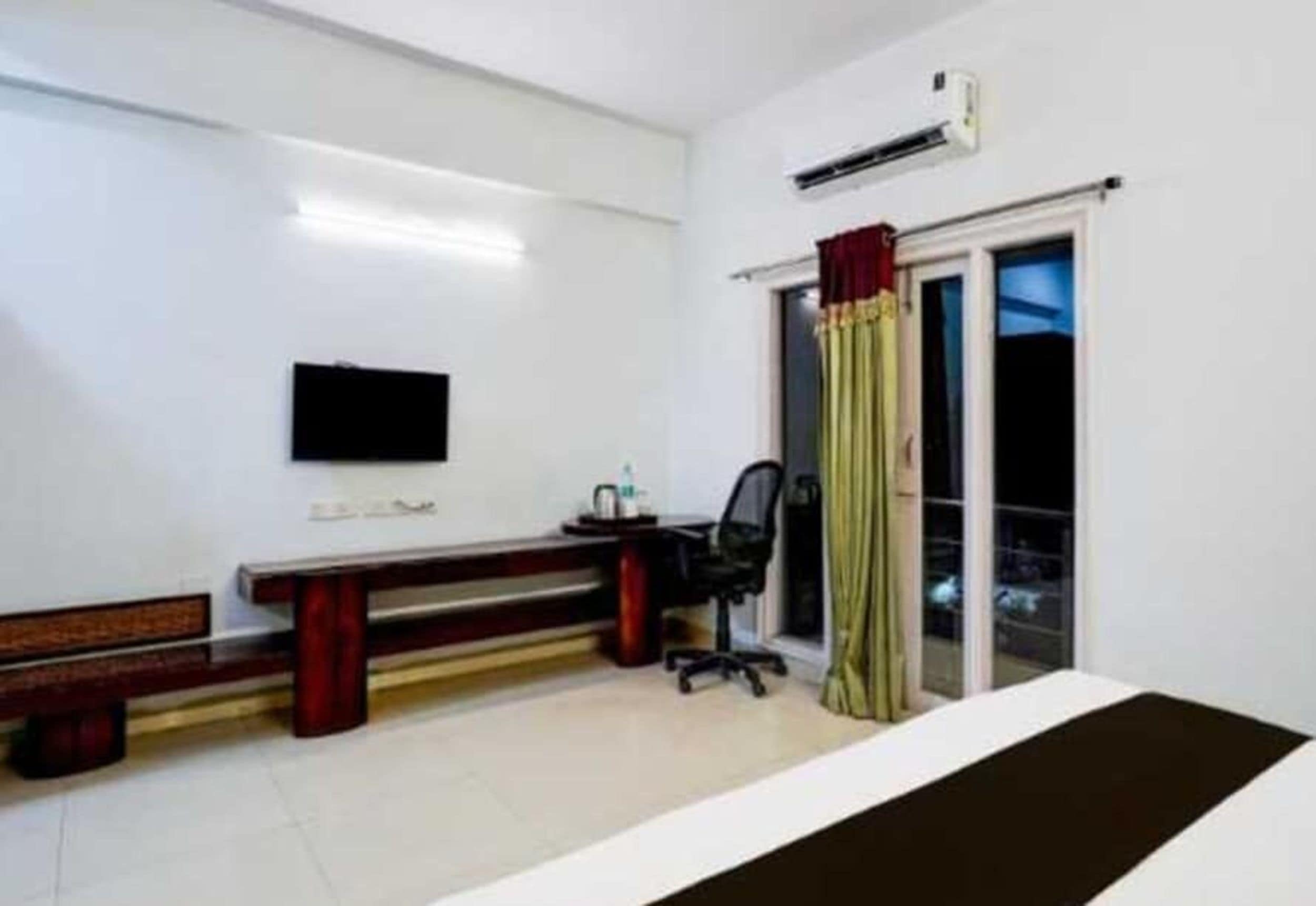 Une chambre dotée d’un téléviseur à écran plat fixé au mur, d’un bureau avec une chaise et d’une fenêtre avec des rideaux.