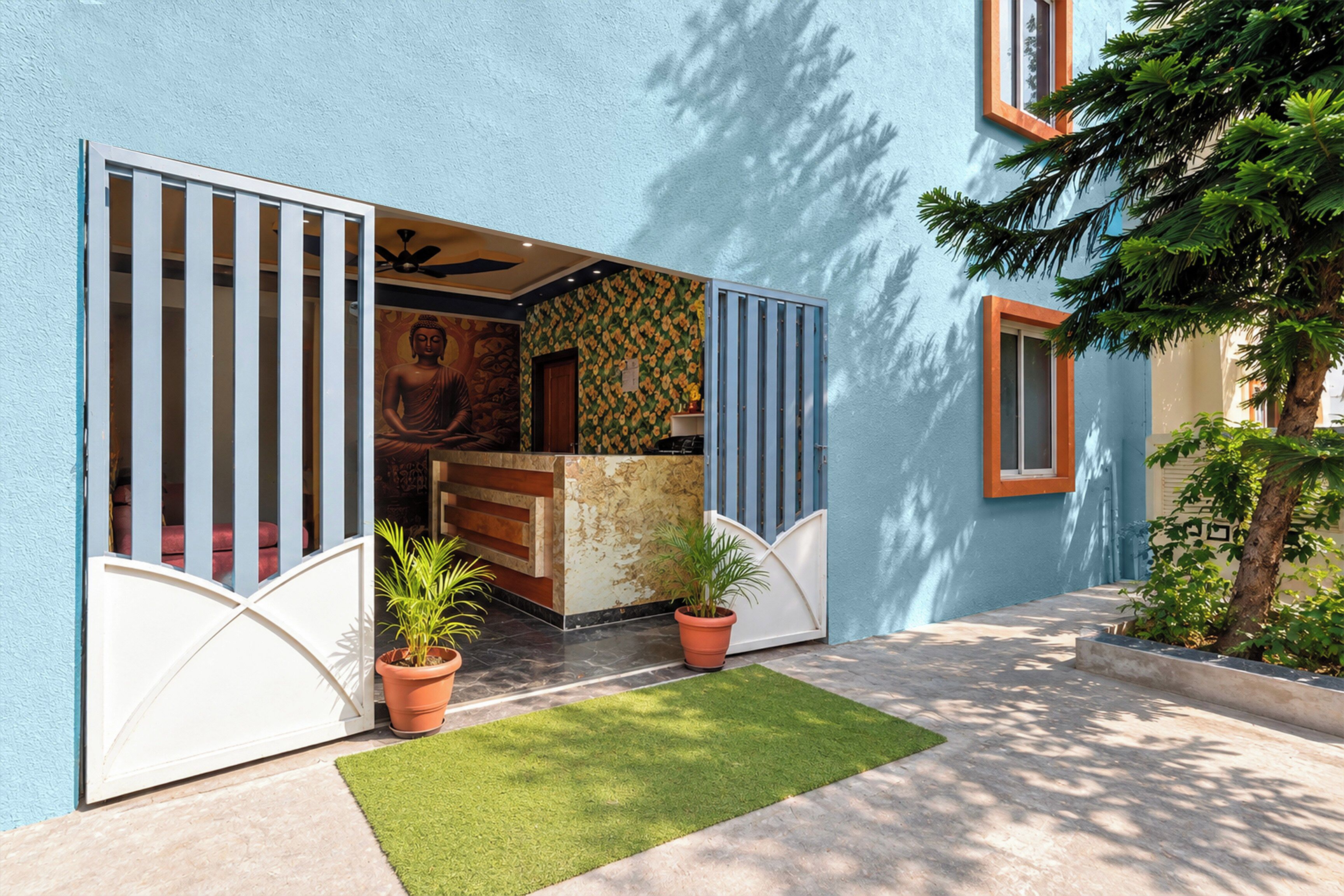 A building entrance with a blue exterior, a Buddha statue, and two potted plants.