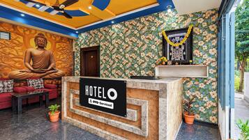 A hotel reception area with a Buddha statue, a sofa, a reception desk, and a floral wall.