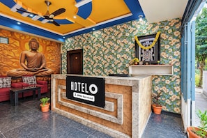 Een hotel receptie met een Boeddhabeeld, een bank, een receptiebalie en een bloemenwand.