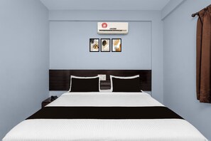 Una habitación de hotel con una cama, aire acondicionado de pared y tres cuadros enmarcados.