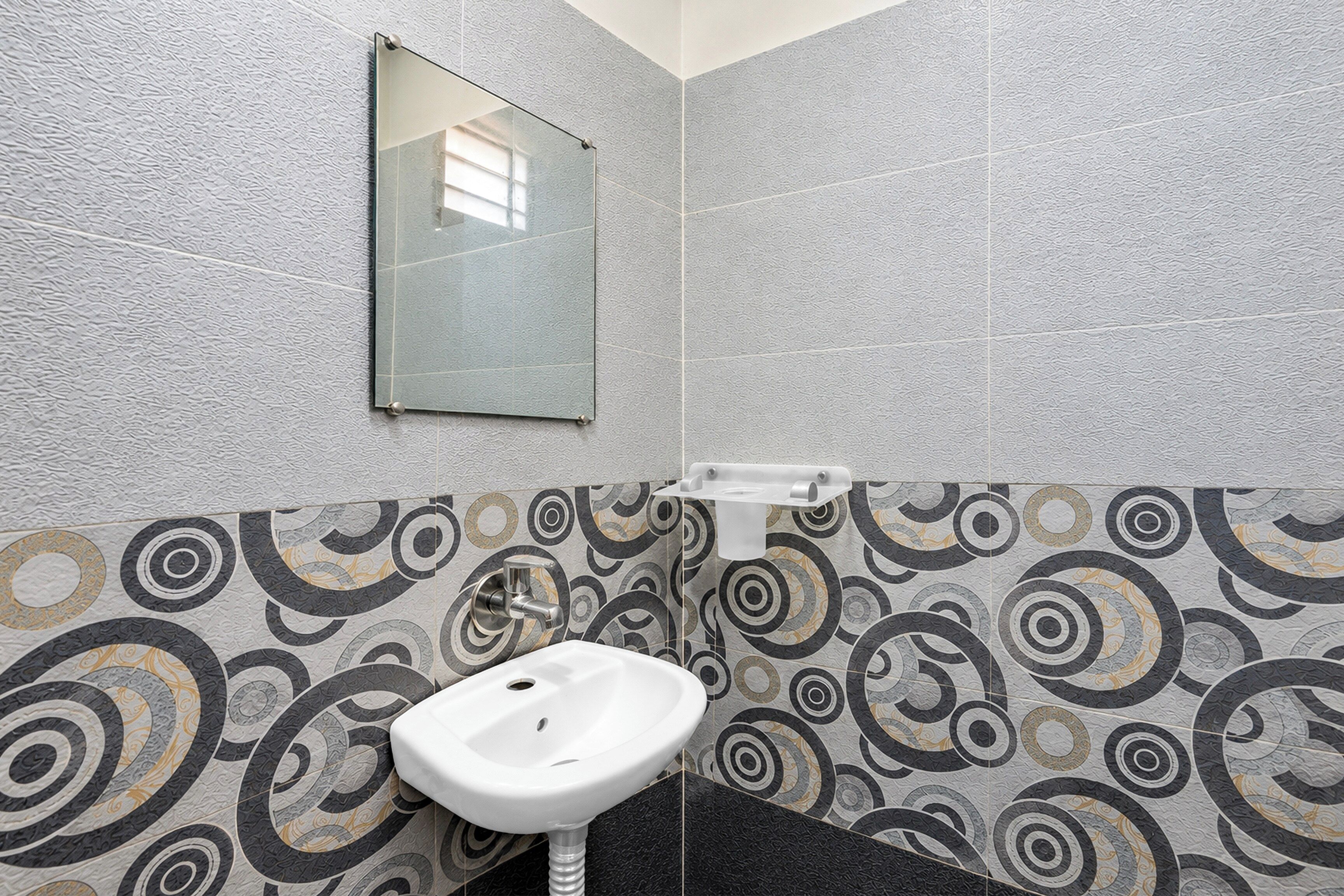 A bathroom with a white sink, a mirror, and patterned wall tiles.