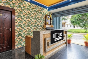 Una recepción de hotel con papel tapiz floral, una puerta de madera y un cartel que indica que el hotel cuenta con servicio de Oyo.
