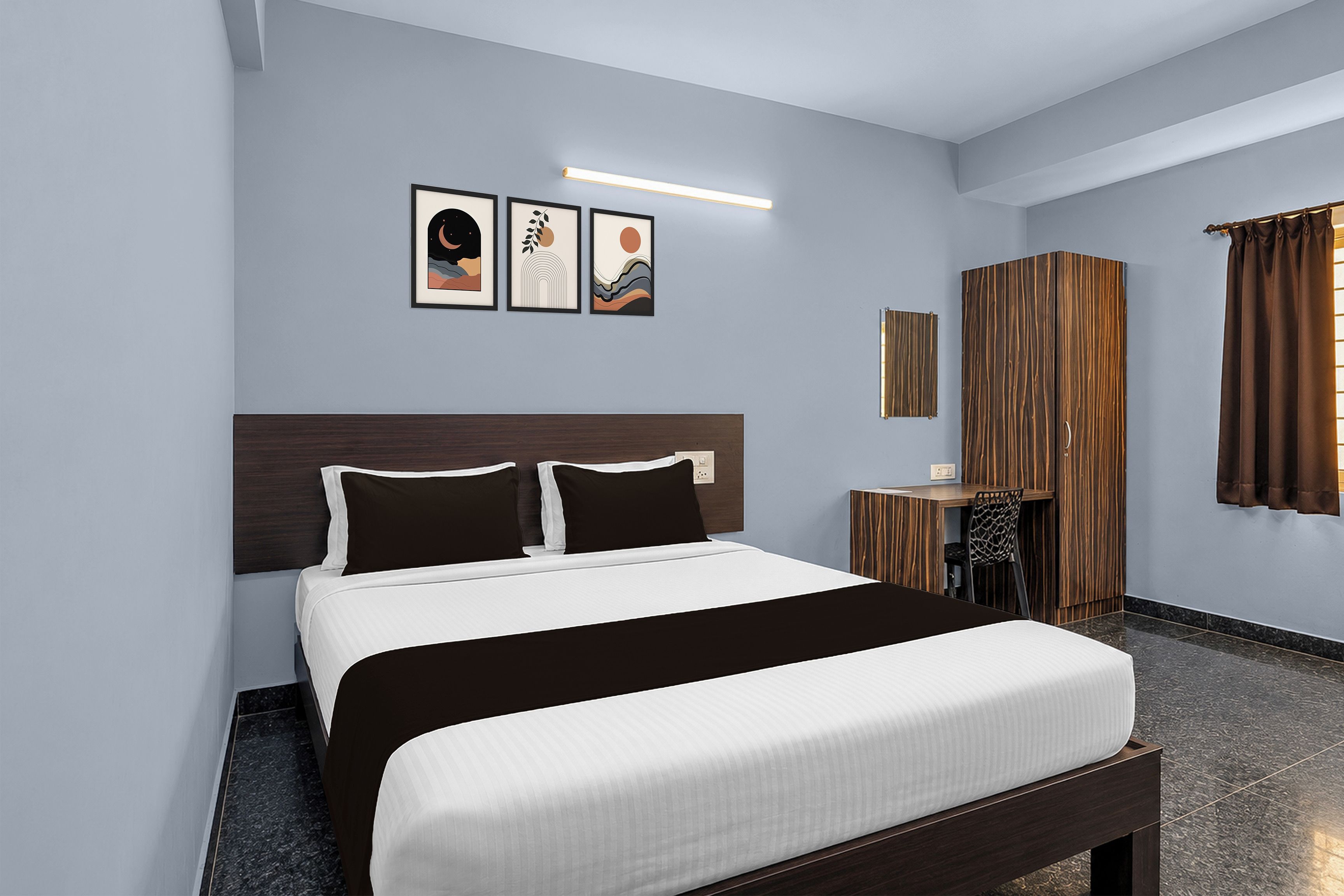 A modern hotel room with a large bed, a wooden headboard, a small desk, a chair, and a window with curtains.