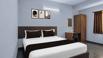 A modern hotel room with a large bed, a wooden headboard, a small desk, a chair, and a window with curtains.