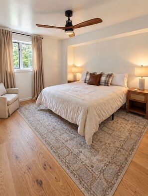 Een slaapkamer met een groot bed, een plafondventilator, een nachtkastje met een lamp en een stoel.