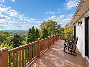 A wooden deck with a railing, a rocking chair, and a view of a forested landscape. - Mountain views, Family friendly, 4 Bed and 3 Bath Home Near Windham Mountain (Acra)