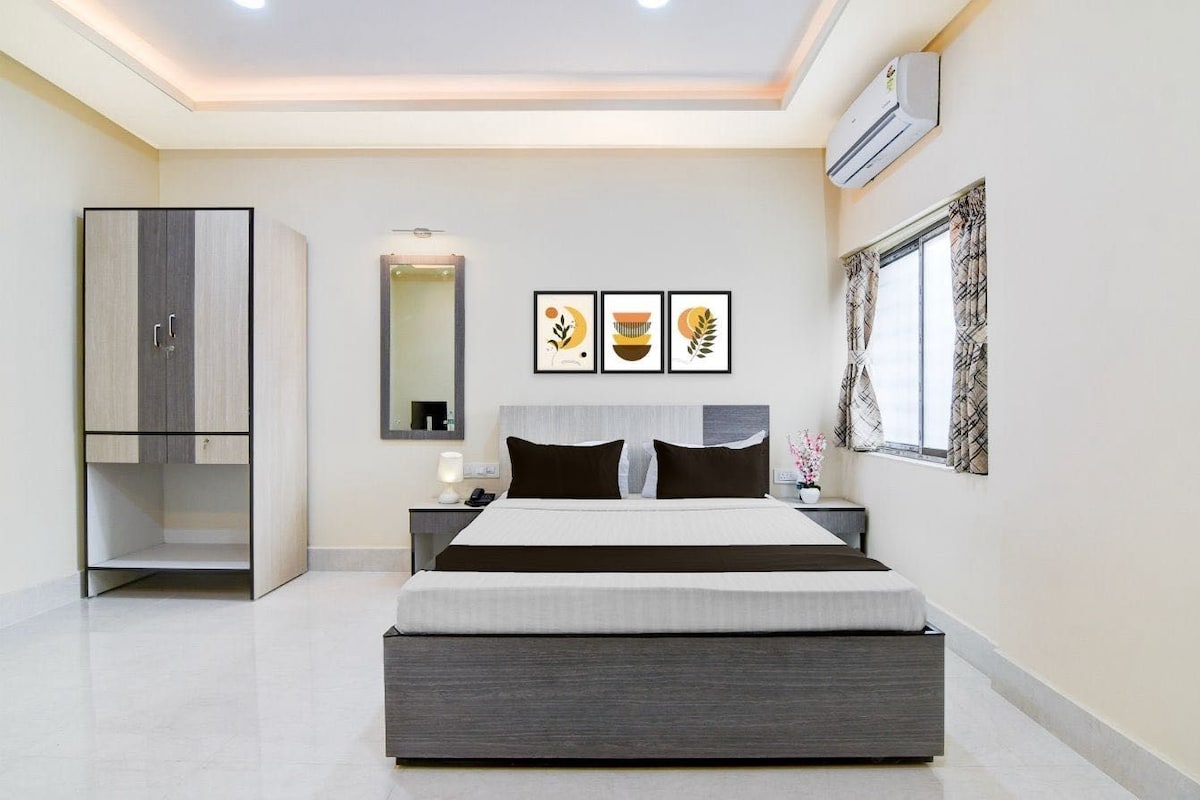 A modern bedroom with a large bed, a wardrobe, a bedside table, a mirror, and framed artwork on the wall.