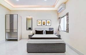 A modern bedroom with a large bed, a wardrobe, a bedside table, a mirror, and framed artwork on the wall.