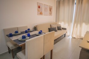 A dining area with a table set for four, a sofa, and a window with curtains. - MG01J  Bella V.  Ap. 105 B  Andres Sardi (Ipojuca)