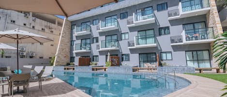 A modern hotel with a swimming pool, outdoor seating, and a view of the building's exterior.