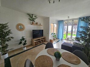 Sala de estar com televisão, assentos e vista para o exterior.