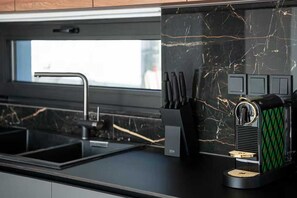 A modern kitchen with a black marble backsplash, a stainless steel sink, and a coffee machine. - Sea-View Villa with Rooftop Hot Tub (Crete)