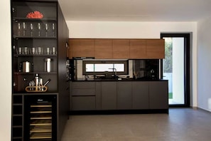 A modern kitchen with dark cabinetry, a built-in oven, and a window overlooking a garden. - Sea-View Villa with Rooftop Hot Tub (Crete)
