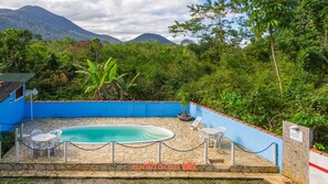 A pool area with a stone deck, surrounded by a blue wall and a rope barrier. - Suite em Ubatuba a 400m da Praia Itamambuca (Ubatuba)