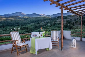 A terrace with two wooden chairs, a table with a white tablecloth, a bottle, glasses, and a lantern. - Peaceful Pool Villa in Crete Countryside (Crete)