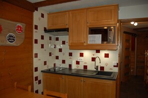 A compact kitchen with wooden cabinets, a black countertop, and a microwave. - Vrbo Property (Châtel)