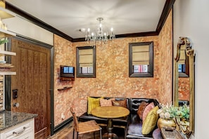 A room with a wooden door, a round table, a sofa with cushions, a television, and a chandelier. - The Lover's Carriage | Jacuzzi for Two (Savannah)