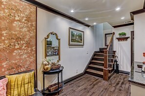 A hallway with a staircase, a decorative mirror, a framed picture, and a console table with a vase. - The Lover's Carriage | Jacuzzi for Two (Savannah)