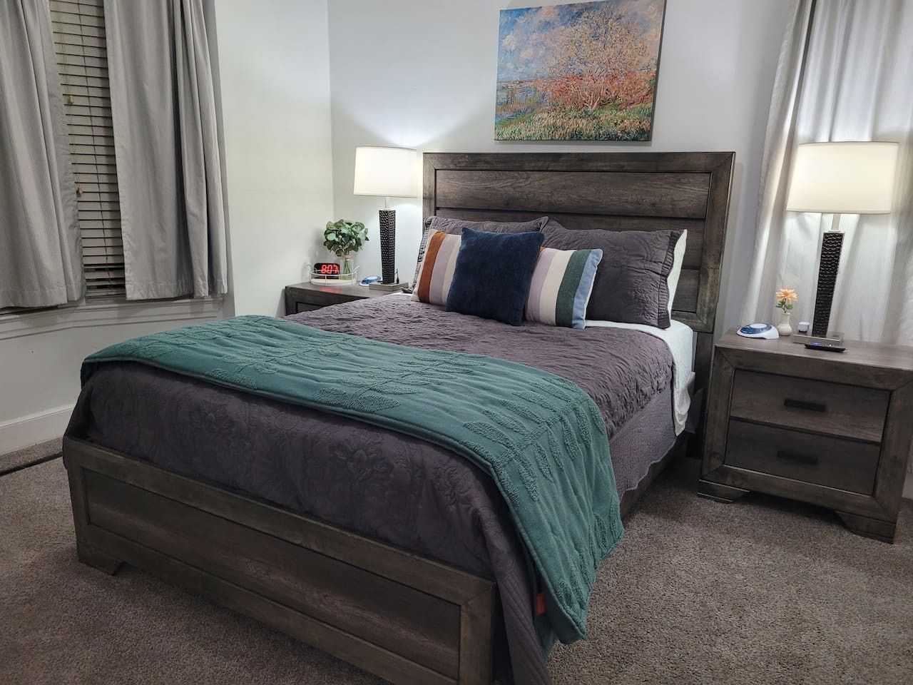 A bedroom with a bed, nightstands, a lamp, a clock, and a painting on the wall.