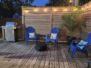 Eine Holzterrasse mit blauen Stühlen, einem Grill und Lichterketten.