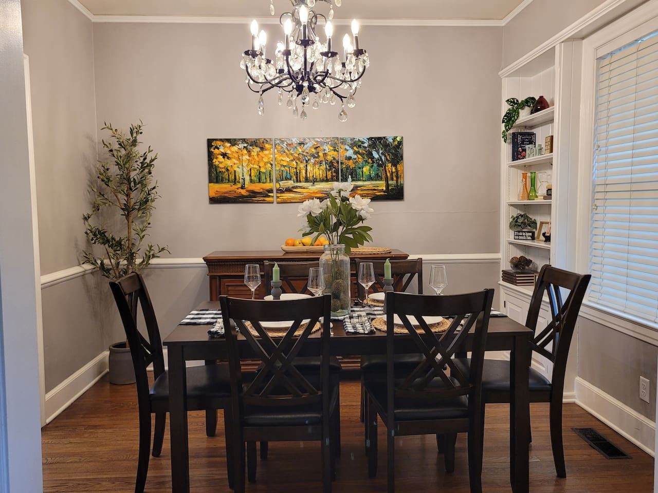 Une salle à manger avec un lustre, un tableau et une bibliothèque.