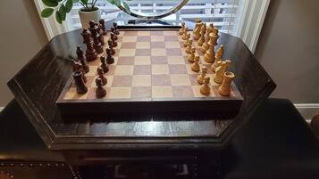 A chessboard set up on a dark wooden table with a potted plant beside it.