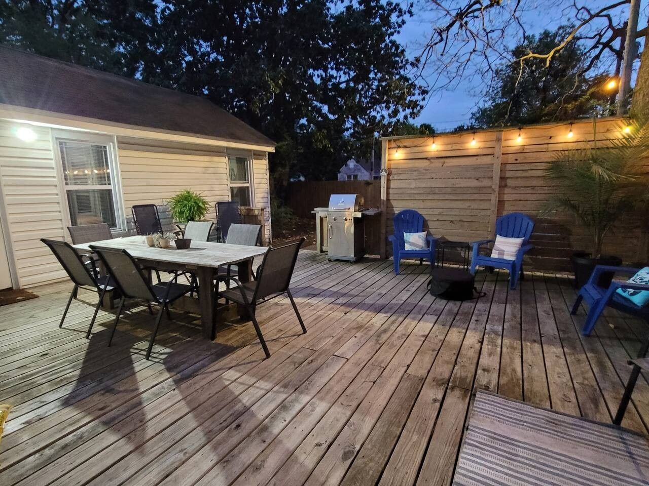 A wooden deck with a dining table and chairs, a grill, and string lights.