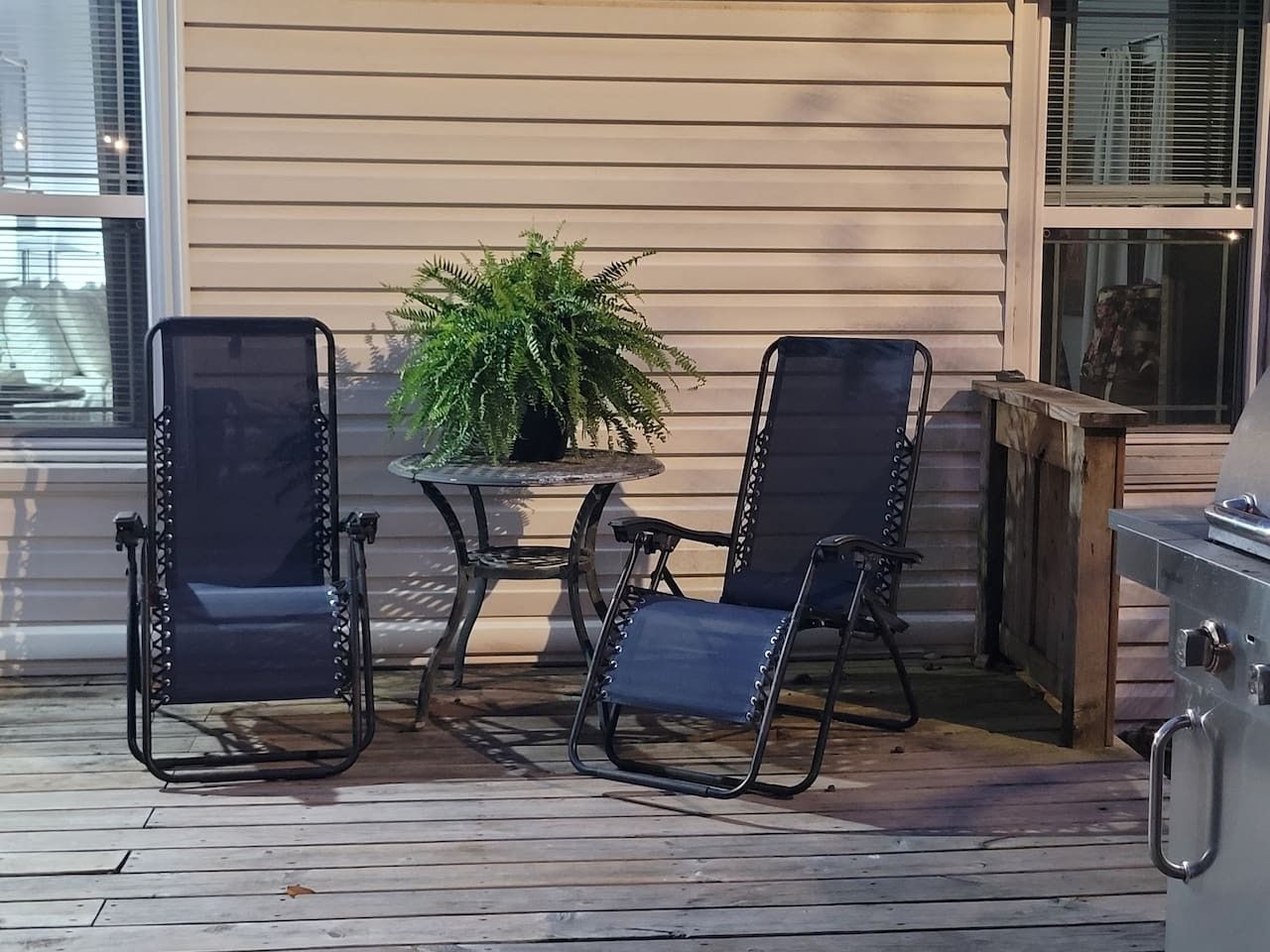 En terrasse med to stole, et bord, en potteplante og en grill.