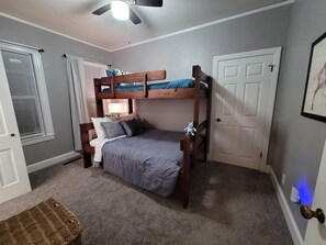 A bedroom with a bunk bed, a bedside table, a lamp, a door, and a window with blinds. - Park Hill Retreat Dog Friendly (Fort Smith)