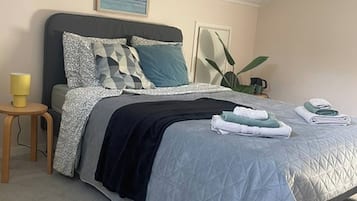 A bedroom with a bed, bedside table, lamp, and a plant.