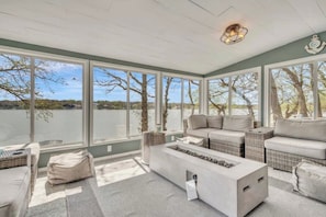 A sunroom with large windows overlooking a body of water, furnished with a sofa, chairs, and a coffee table.