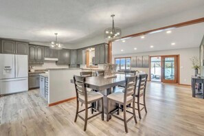 A spacious kitchen with a central island, wooden chairs, and pendant lighting.