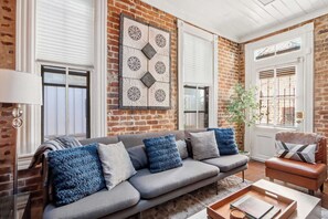 A living room with a grey sofa, a brown leather armchair, and a decorative wall piece. - The Lyons House | Historic Savannah Luxury (Savannah)