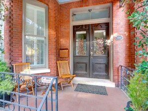 A brick building with a double door entrance, two wooden chairs, and a metal railing. - The Lyons House | Historic Savannah Luxury (Savannah)