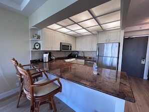 A modern kitchen with white cabinets, stainless steel appliances, and a central island with seating. - Ocean View One Bedroom, Two Bath Condo - Steps from Beach - The Whaler 624 (Lahaina)