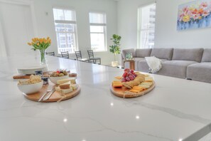 A modern kitchen with a marble countertop, a dining table with plates and cutlery, and a sofa in the background. - Ocean Views • Private Pool and Spa • 12 Sleeping Rooms • Sleeps 28 (North Myrtle Beach)