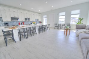 A modern kitchen with white cabinets, a central island with bar stools, and a dining area with chairs. - Ocean Views • Private Pool and Spa • 12 Sleeping Rooms • Sleeps 28 (North Myrtle Beach)