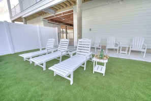 A patio area with white lounge chairs and a small table, surrounded by a white fence and a building with a balcony. - Ocean Views • Private Pool and Spa • 12 Sleeping Rooms • Sleeps 28 (North Myrtle Beach)