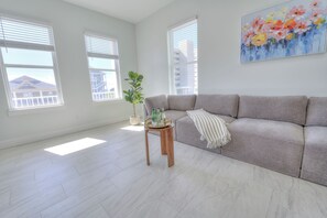 Uma sala de estar ampla com um sofá cinzento, uma pequena mesa lateral de madeira e uma planta em vaso.