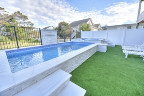 A swimming pool with a stone edge, surrounded by a white fence, and a grassy area with white lounge chairs. - Ocean Views • Private Pool and Spa • 12 Sleeping Rooms • Sleeps 28 (North Myrtle Beach)