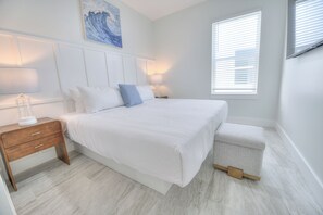 A bedroom with a large bed, bedside tables, a nightstand, a window with blinds, and a wall-mounted artwork. - Ocean Views • Private Pool and Spa • 12 Sleeping Rooms • Sleeps 28 (North Myrtle Beach)