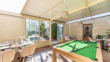 A pool table in a room with large windows, a dining area, and a stone wall.