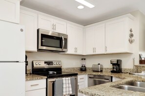 A modern kitchen with white cabinets, stainless steel appliances including a microwave, stove, and toaster, and a granite countertop. - 🌴Snapper Landing | Steps to Beach | Pool | Pet Friendly🌴 (Mexico Beach)