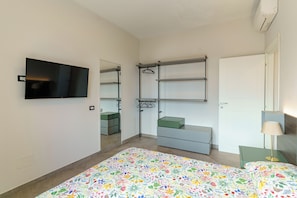 Un dormitorio con cama, televisor, armario, escritorio y lámpara.
