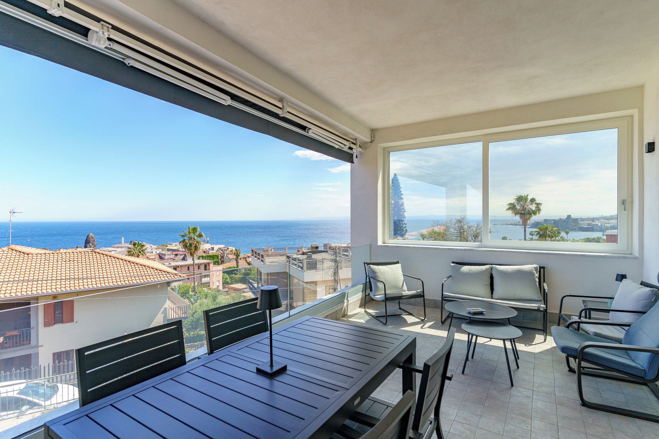 Ein Balkon mit Blick auf das Meer und die Stadtlandschaft, ausgestattet mit einem Tisch, Stühlen und einer Lampe.