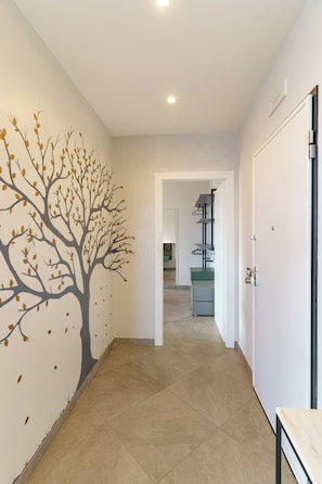 Un pasillo con un mural de un árbol, una puerta y una zona de cocina al fondo.